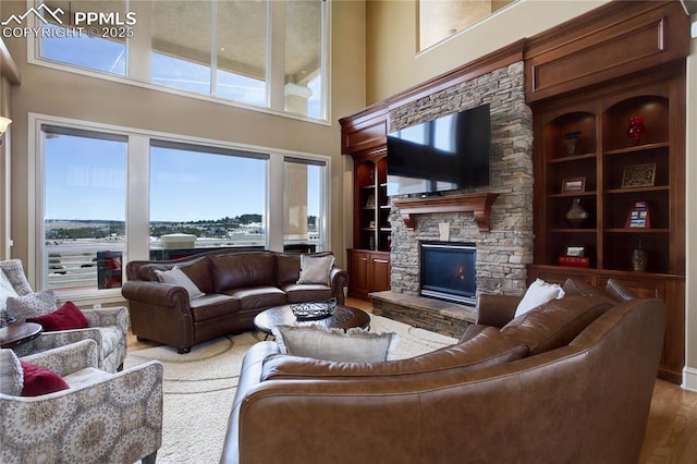 living room featuring built in shelves, wood-type flooring, a fireplace, and a high ceiling