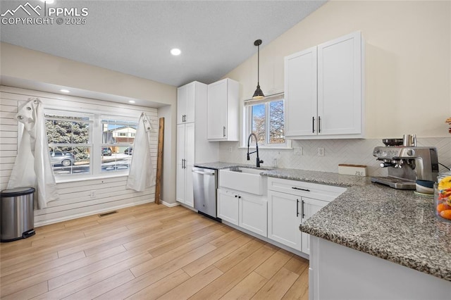 kitchen with sink, light stone countertops, white cabinets, decorative light fixtures, and stainless steel dishwasher