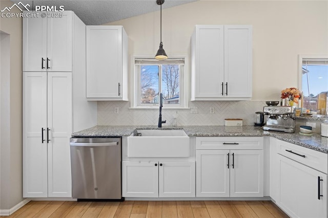 kitchen featuring pendant lighting, white cabinetry, sink, stainless steel dishwasher, and light stone counters