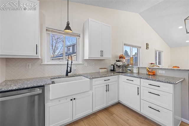 kitchen with tasteful backsplash, dishwasher, lofted ceiling, sink, and white cabinets