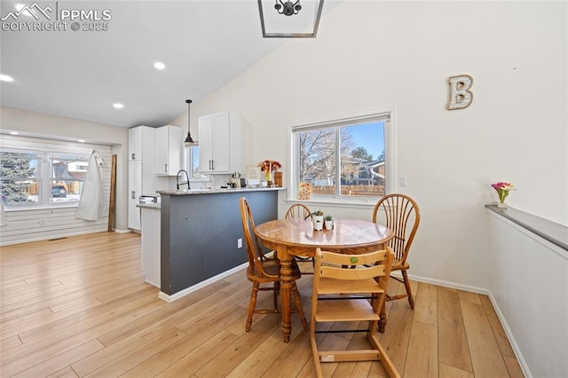 dining room featuring lofted ceiling, sink, and light hardwood / wood-style flooring