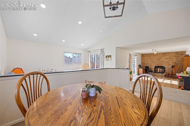 dining room with lofted ceiling, a stone fireplace, and light hardwood / wood-style floors