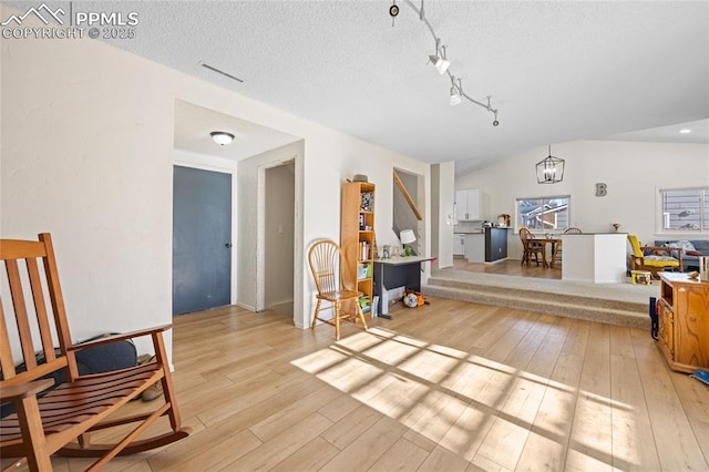 sitting room with a notable chandelier, vaulted ceiling, a textured ceiling, and light hardwood / wood-style floors