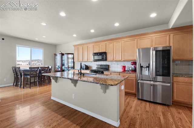 kitchen with sink, range, dark stone countertops, stainless steel refrigerator with ice dispenser, and a center island with sink