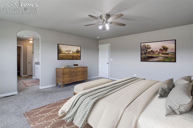 carpeted bedroom with connected bathroom, arched walkways, baseboards, and a ceiling fan