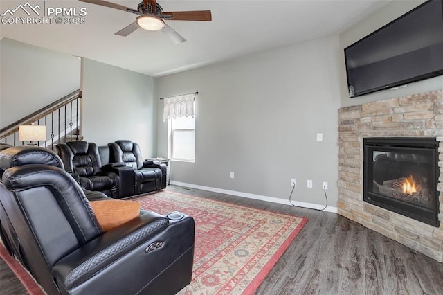 living area featuring a stone fireplace, baseboards, ceiling fan, and wood finished floors