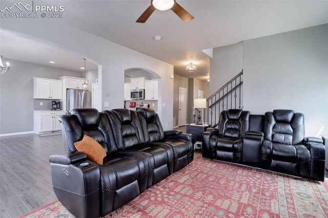 living room with arched walkways, ceiling fan with notable chandelier, and wood finished floors