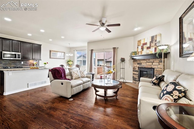 living room with a stone fireplace, dark wood-type flooring, and ceiling fan