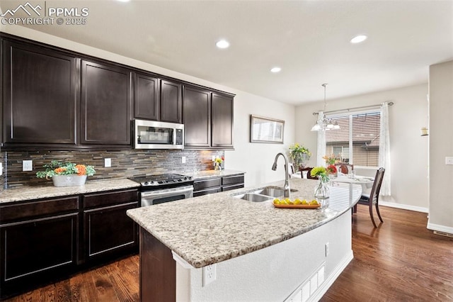 kitchen with sink, tasteful backsplash, decorative light fixtures, appliances with stainless steel finishes, and an island with sink