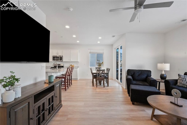 living room with ceiling fan, sink, and light hardwood / wood-style floors