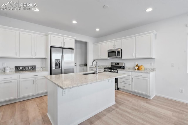 kitchen featuring appliances with stainless steel finishes, white cabinetry, sink, light stone counters, and a center island with sink