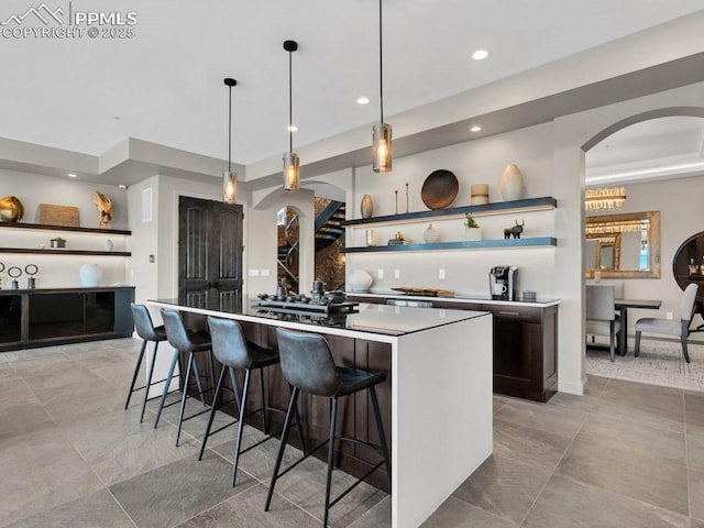 kitchen with arched walkways, open shelves, a kitchen island, a kitchen bar, and recessed lighting