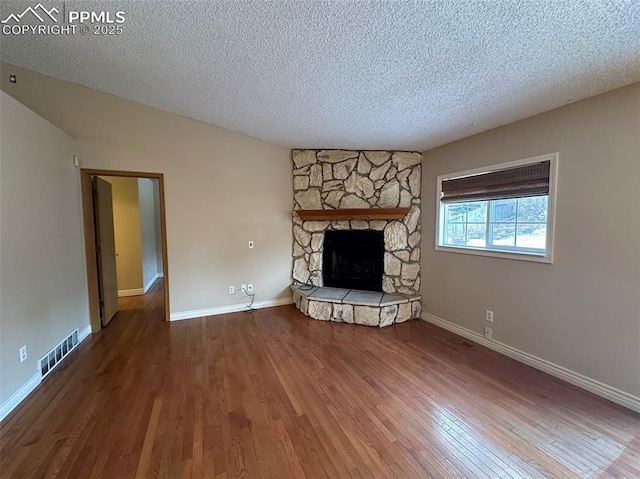 unfurnished living room with a stone fireplace, a textured ceiling, and hardwood / wood-style flooring