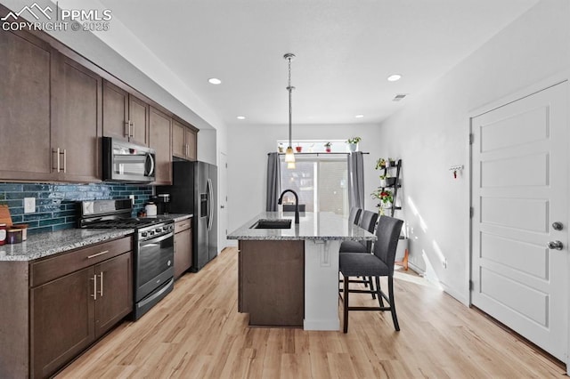 kitchen with a kitchen bar, sink, light stone counters, an island with sink, and stainless steel appliances