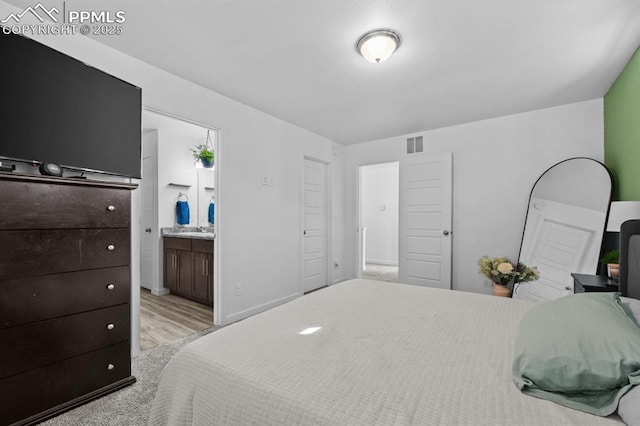 bedroom with connected bathroom, sink, and light wood-type flooring