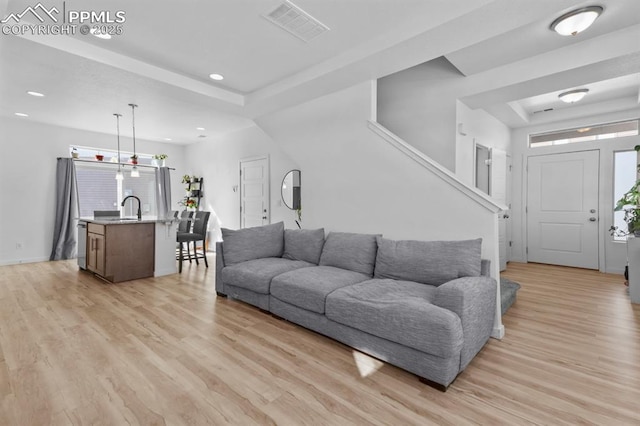 living room with sink, a raised ceiling, and light hardwood / wood-style floors