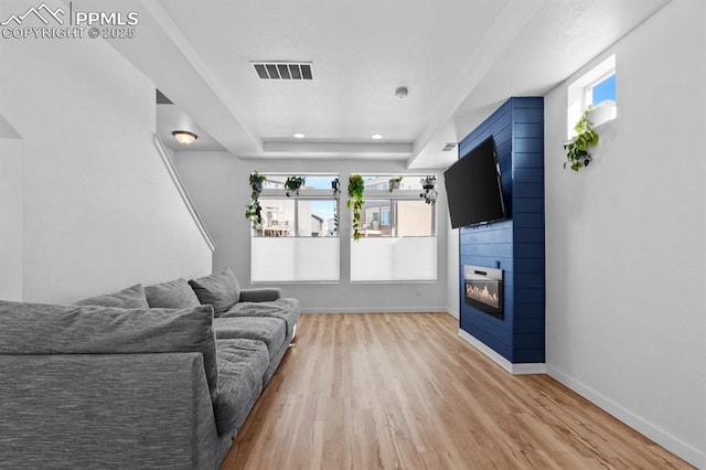 living room featuring a large fireplace, a raised ceiling, and light wood-type flooring