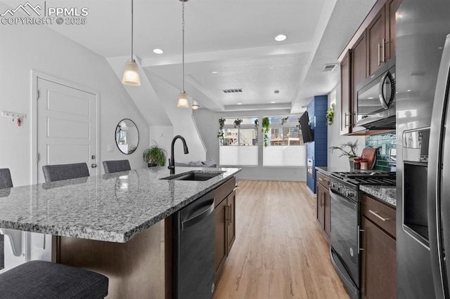 kitchen with a kitchen bar, sink, a center island with sink, pendant lighting, and black appliances