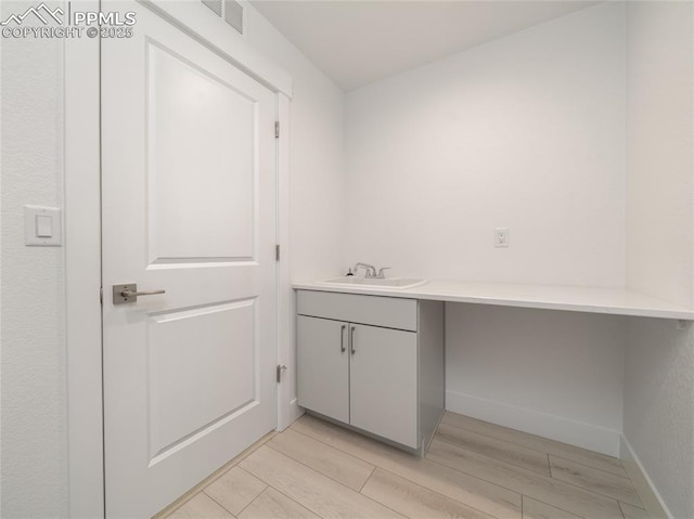 washroom with a sink, visible vents, baseboards, and light wood-style floors