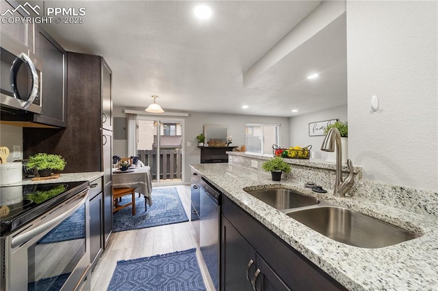 kitchen with stainless steel appliances, light stone countertops, sink, and dark brown cabinetry