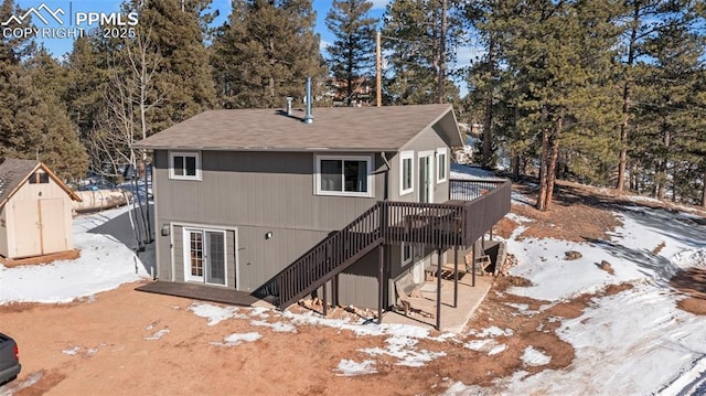 snow covered rear of property featuring a wooden deck and a shed