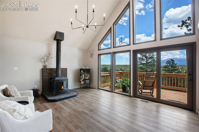 living room featuring a high ceiling, a wood stove, a chandelier, and light wood-type flooring