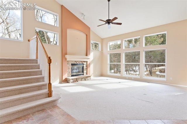 unfurnished living room with ceiling fan, a stone fireplace, light carpet, and high vaulted ceiling