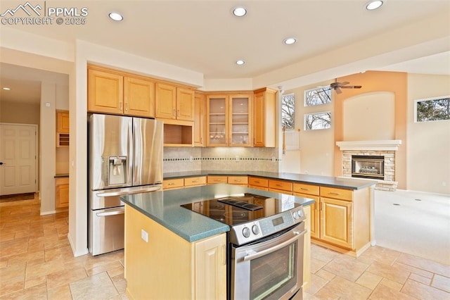 kitchen featuring a stone fireplace, a center island, light brown cabinets, stainless steel appliances, and backsplash