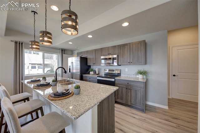 kitchen with pendant lighting, a kitchen island with sink, light stone countertops, and appliances with stainless steel finishes