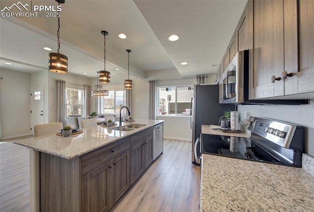 kitchen with pendant lighting, sink, light hardwood / wood-style floors, stainless steel appliances, and light stone countertops