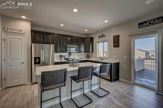 kitchen with a kitchen bar, a center island, stainless steel appliances, dark brown cabinets, and light hardwood / wood-style flooring