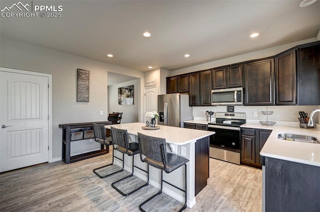 kitchen featuring a breakfast bar, sink, appliances with stainless steel finishes, a kitchen island, and light hardwood / wood-style floors
