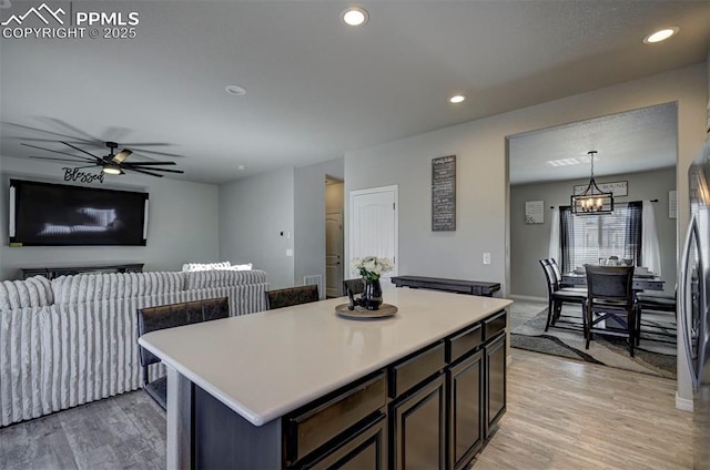 kitchen with decorative light fixtures, ceiling fan with notable chandelier, a center island, and light wood-type flooring