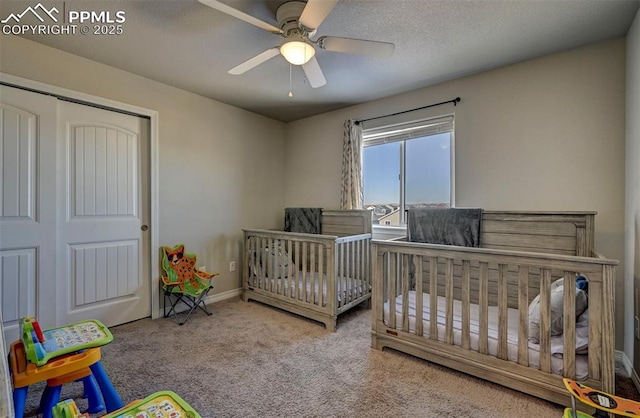 bedroom with a crib, ceiling fan, carpet, a textured ceiling, and a closet