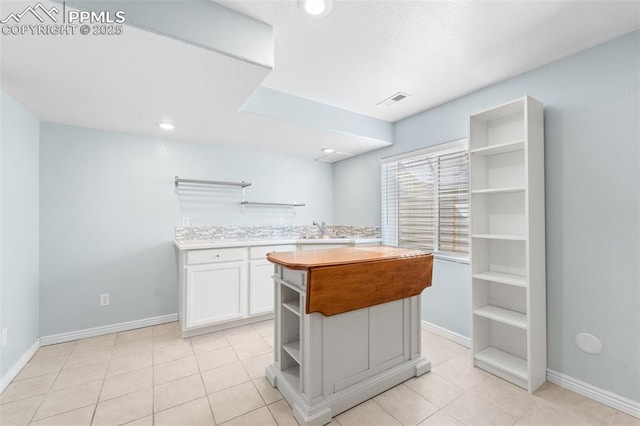 kitchen with light tile patterned flooring, a kitchen island, sink, and white cabinets