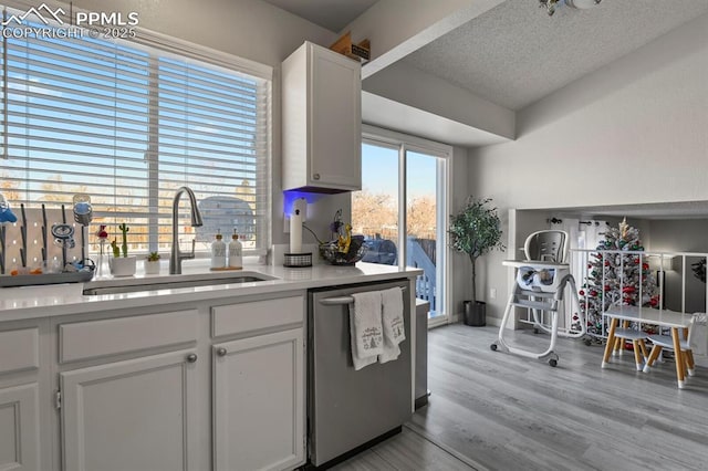 kitchen featuring white cabinetry, sink, light wood-type flooring, stainless steel dishwasher, and a textured ceiling