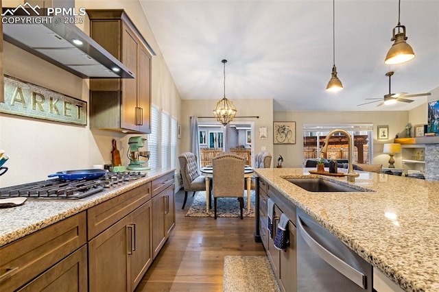 kitchen featuring pendant lighting, sink, stainless steel appliances, light stone countertops, and wall chimney exhaust hood