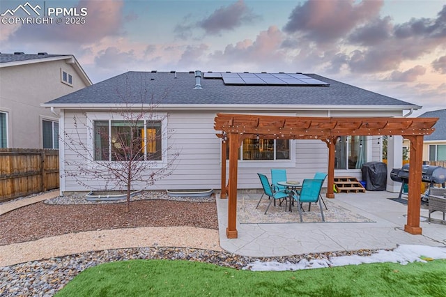 back house at dusk featuring a pergola, a patio, and solar panels