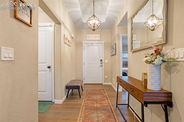 entryway featuring a notable chandelier, a tray ceiling, and light wood-type flooring