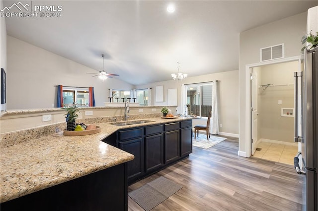 kitchen featuring sink, vaulted ceiling, light wood-type flooring, stainless steel refrigerator, and light stone countertops