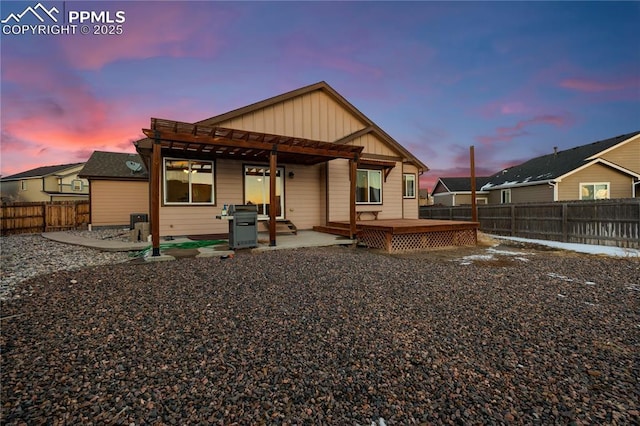 back house at dusk featuring a pergola, a deck, and a patio