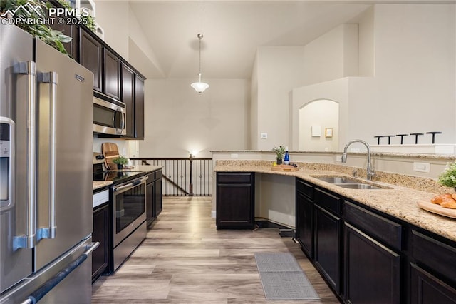 kitchen featuring sink, light stone counters, hanging light fixtures, light hardwood / wood-style flooring, and appliances with stainless steel finishes