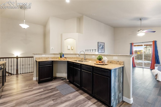 kitchen with decorative light fixtures, sink, light stone counters, a center island with sink, and light hardwood / wood-style flooring