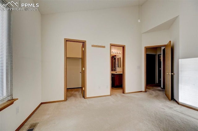 unfurnished bedroom featuring a walk in closet, high vaulted ceiling, ensuite bathroom, and light colored carpet