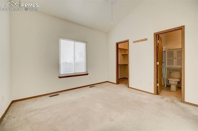 unfurnished bedroom featuring connected bathroom, a spacious closet, high vaulted ceiling, light carpet, and a closet