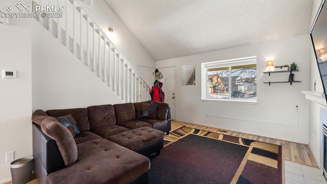 living room with a fireplace with flush hearth, vaulted ceiling, a textured ceiling, and stairs