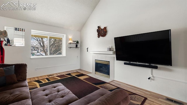 living room with visible vents, a tiled fireplace, wood finished floors, vaulted ceiling, and a textured ceiling