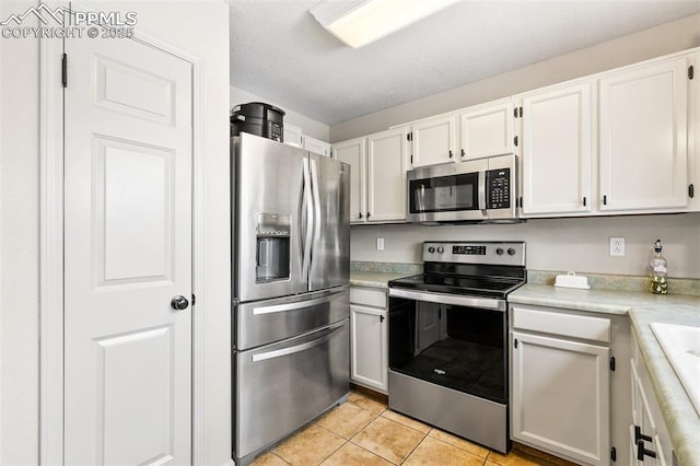 kitchen with stainless steel appliances, light tile patterned floors, and white cabinets