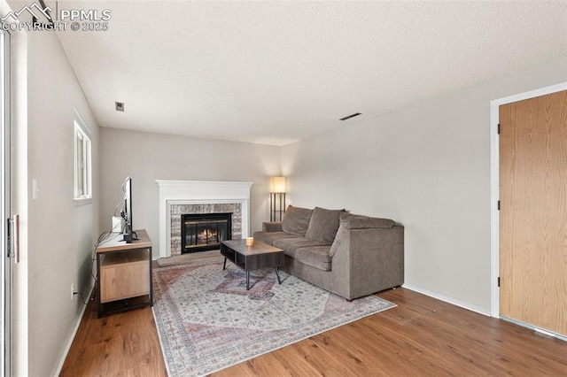 living room featuring a stone fireplace, hardwood / wood-style floors, and a textured ceiling