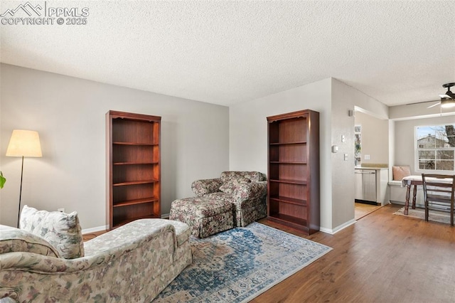 living room featuring ceiling fan, light hardwood / wood-style flooring, and a textured ceiling